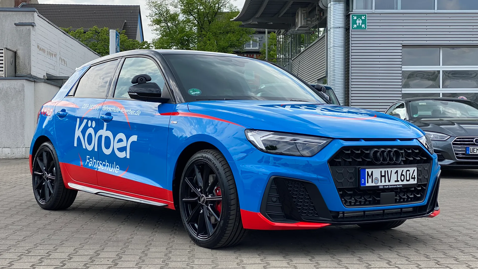 Blauer Audi mit roter Körber-Folierung, von schräg vorne fotografiert